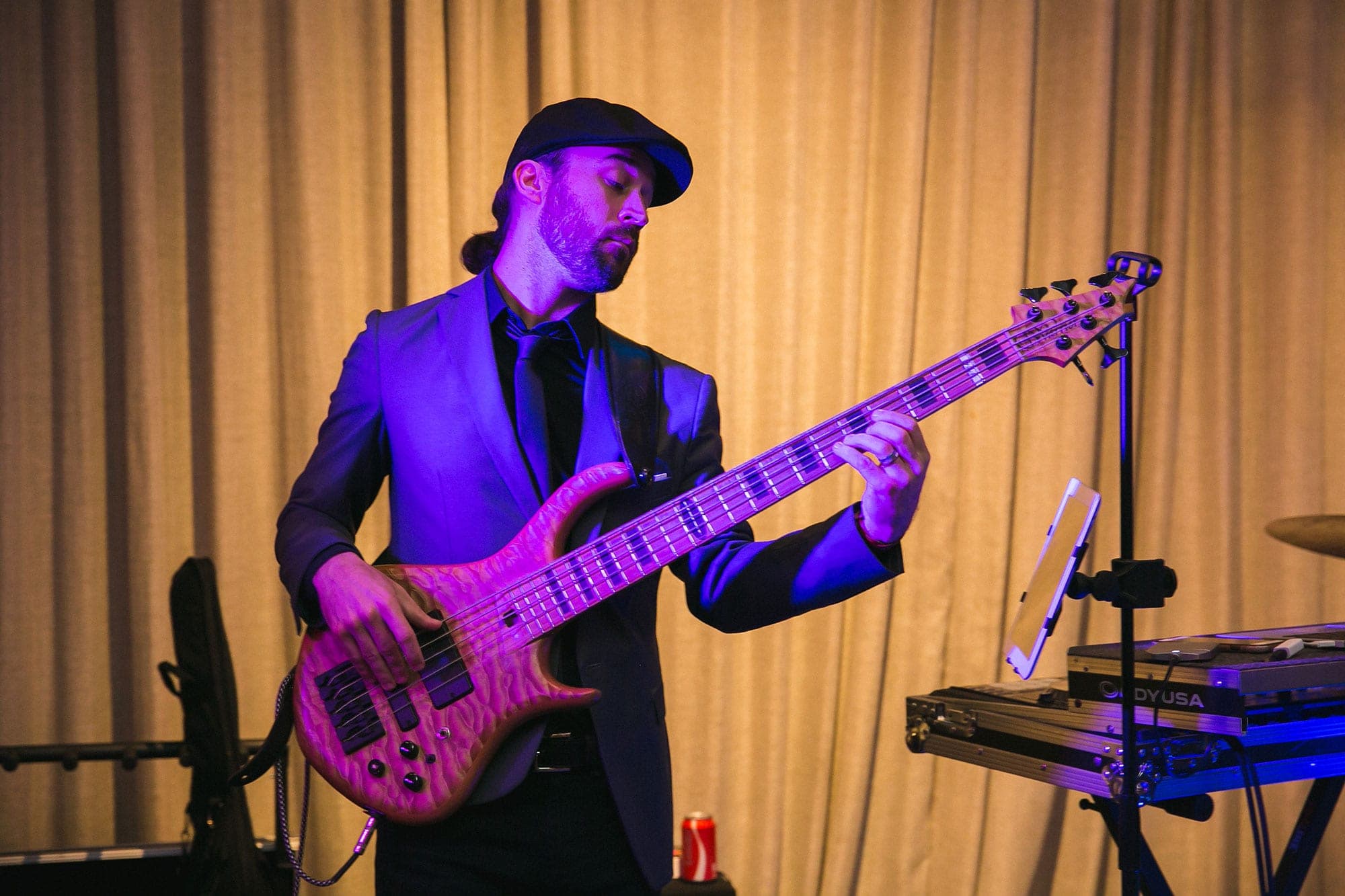 The band's bass player on stage in a flat cap, playing a five-string bass
